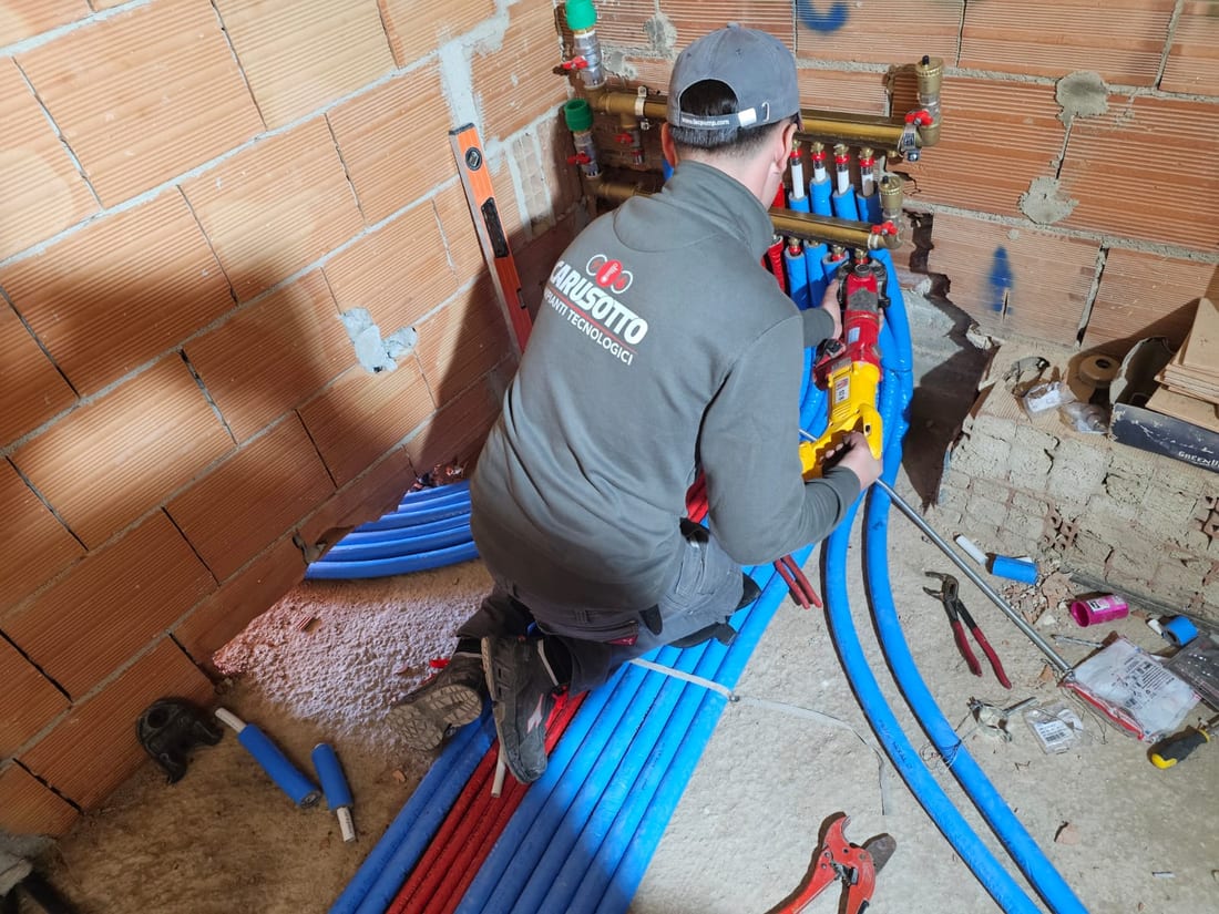 Tecnico di Carusotto Impianti al lavoro su un collettore idraulico con tubazioni blu